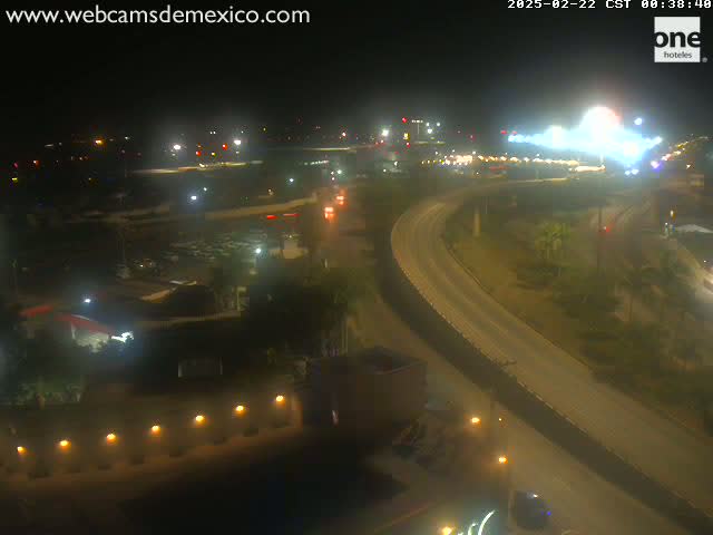 A nighttime, high-angle view shows a highway curving through a landscape of low buildings and sparse vegetation under a clear sky.