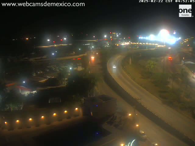 A nighttime, high-angle view of a highway interchange with sparse traffic, surrounded by dimly lit buildings and landscaping.