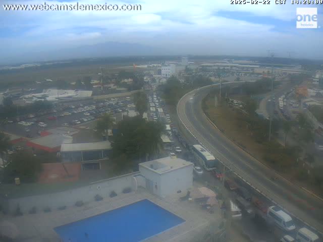An elevated view shows a partly cloudy day with a highway curving past an airport and parking lots, leading to heavy traffic congestion.