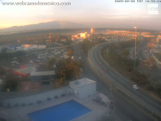 A hazy sunset view overlooking a highway, airport, parking lots, and a building with a swimming pool.