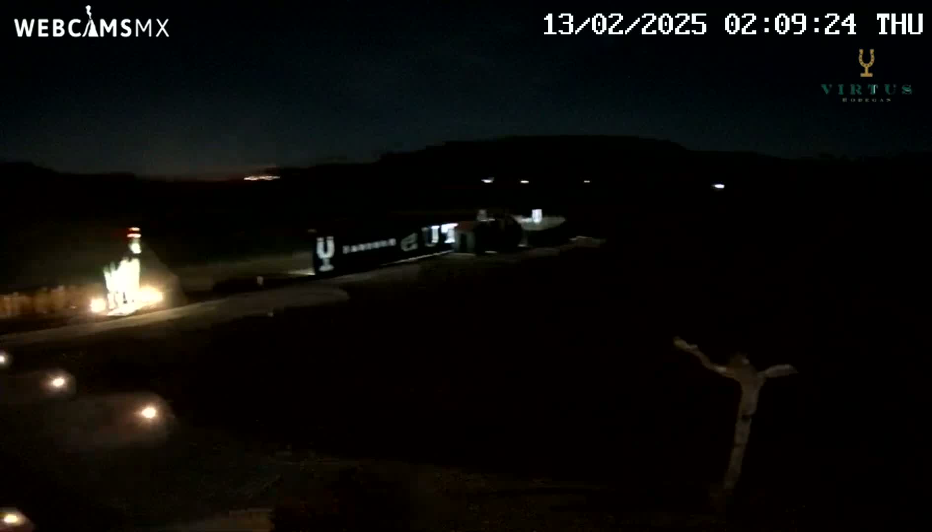 A nighttime, low-light view of a dark road with dimly lit areas and a few lights visible in the distance.