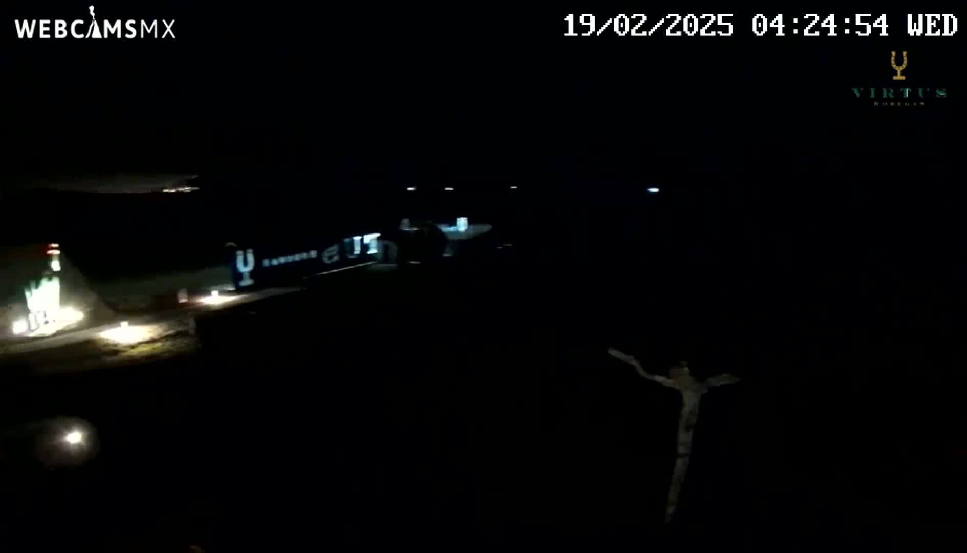 A dark nighttime scene shows a partially illuminated building and a vaguely humanoid figure, with dim lights visible on the ground.