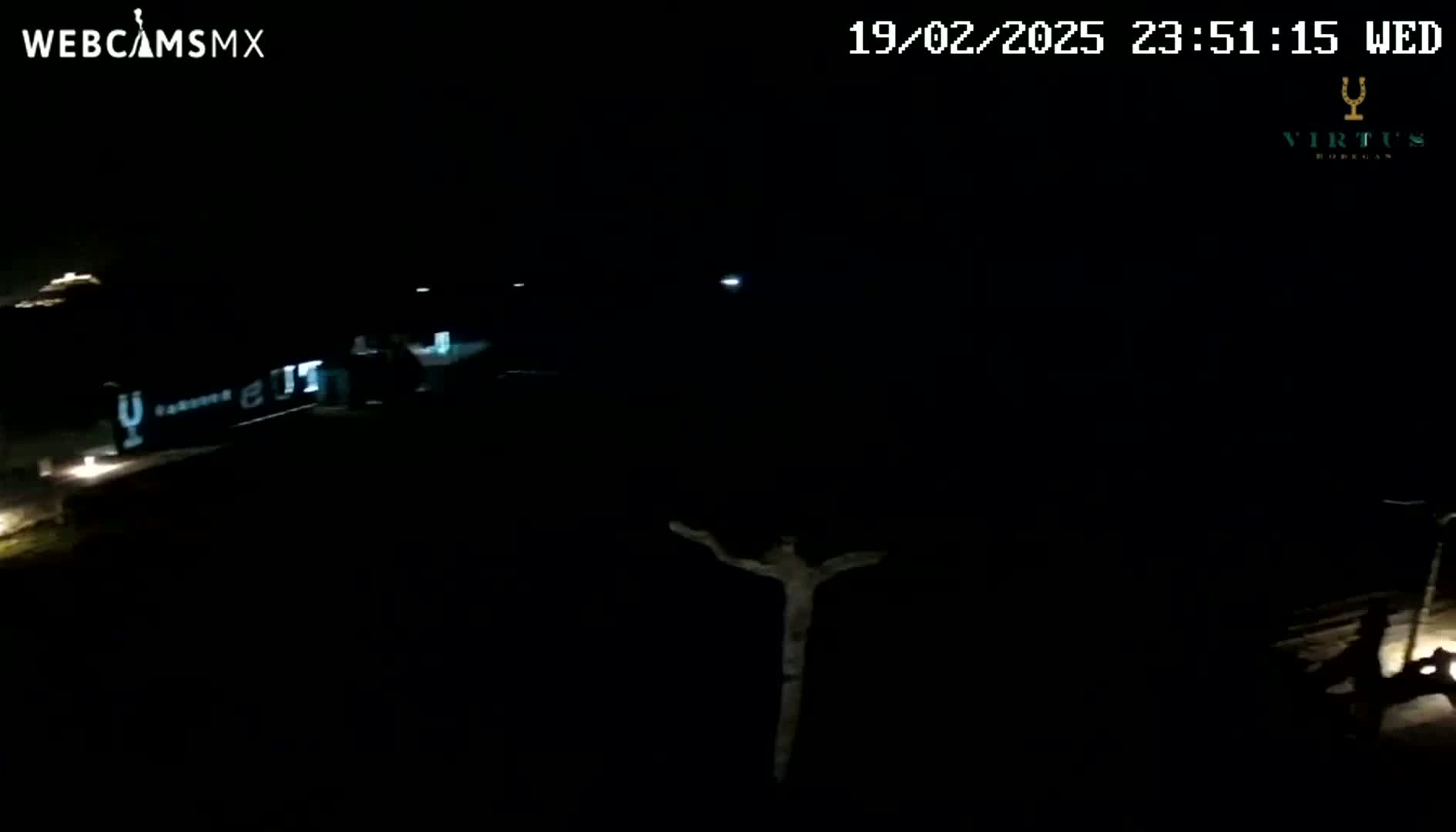 A nighttime, dark outdoor scene shows a dimly lit structure and a cross-shaped object in the foreground.