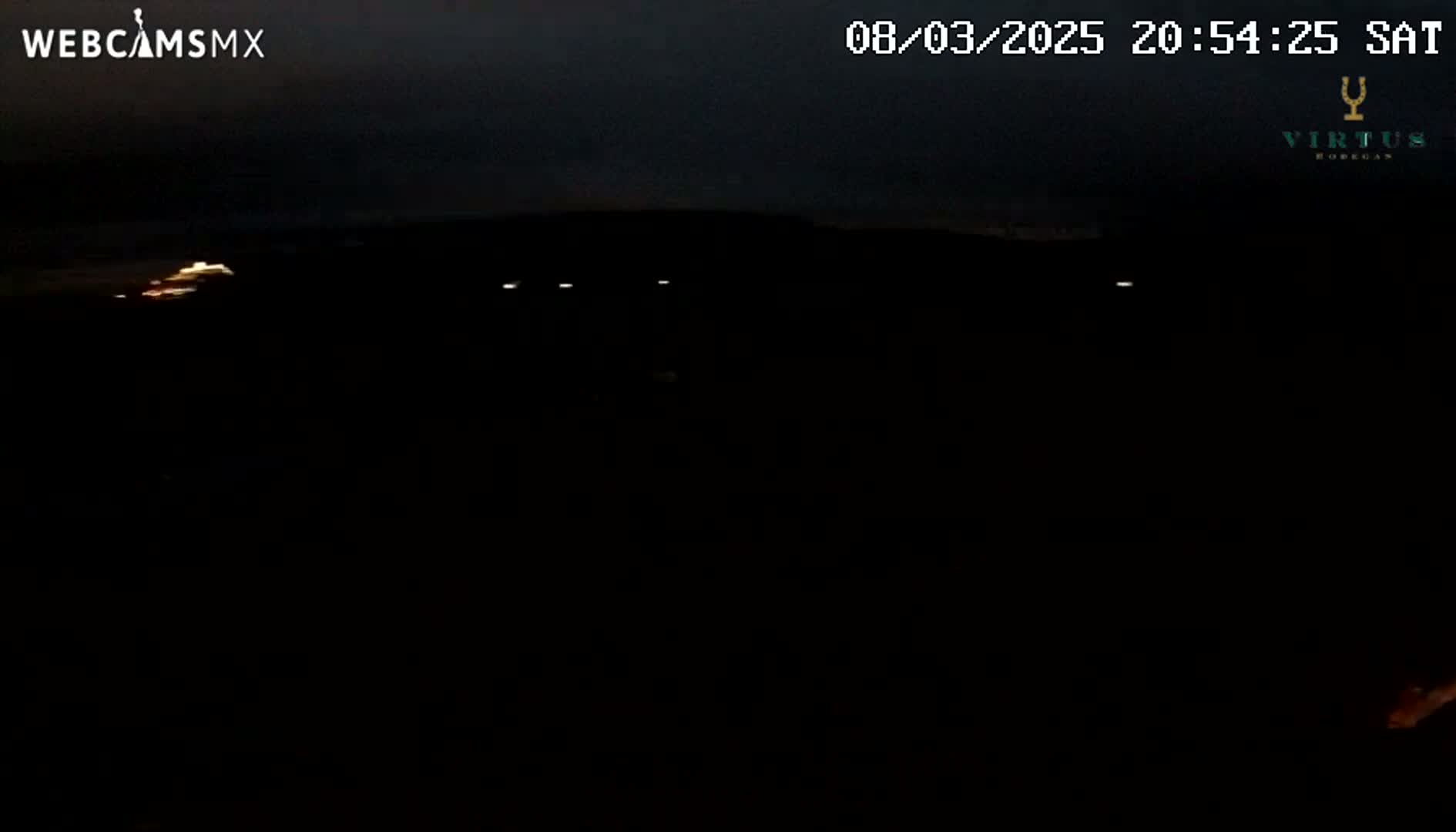 A dark, nighttime scene shows a few faint lights in the distance under a mostly clear sky.