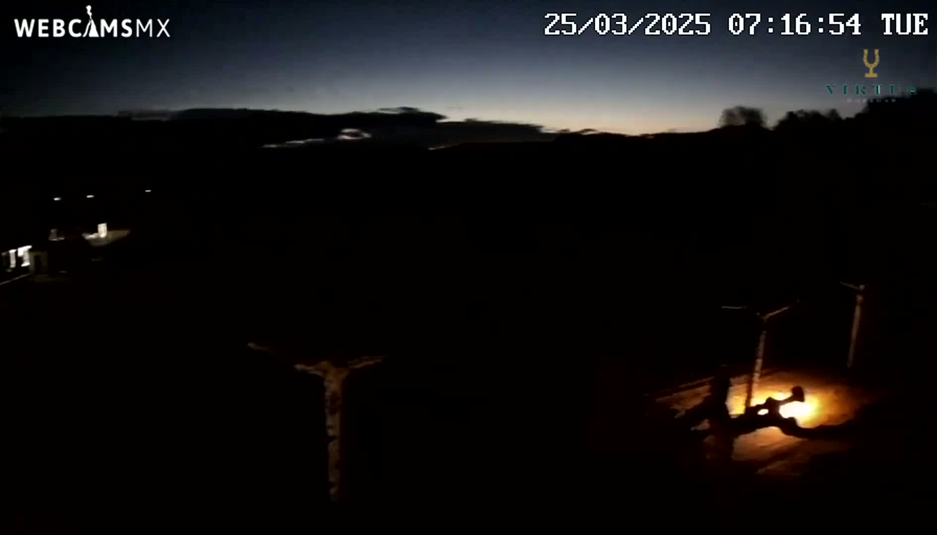 A dark, nighttime scene shows a dimly lit area with a small, bright light source near the bottom, possibly a fire, under a twilight sky.