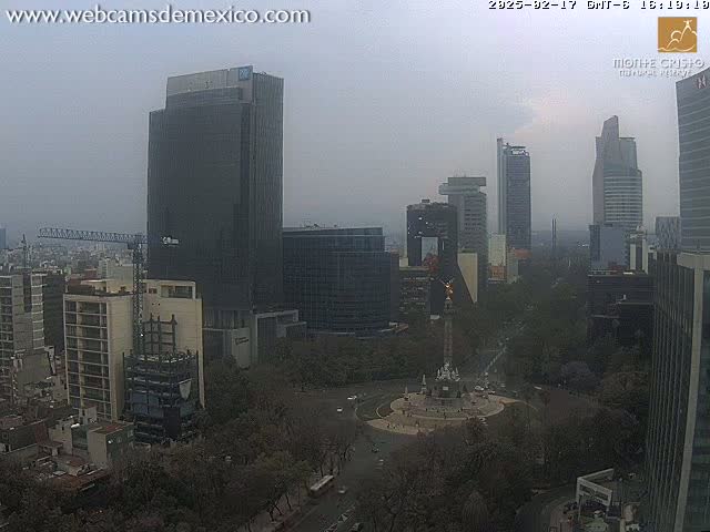 A hazy, overcast city view shows numerous tall buildings surrounding a circular plaza with a monument in the center.
