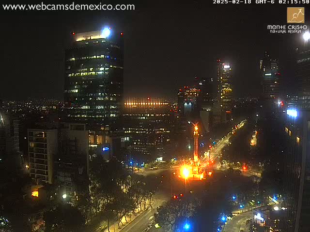 A nighttime view of a city with brightly lit skyscrapers and a monument illuminated in orange and yellow, under a clear, dark sky.
