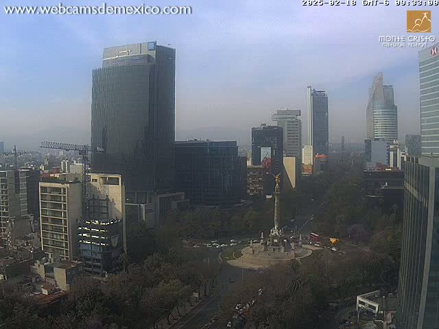 A hazy, daytime view of a cityscape featuring numerous skyscrapers and high-rise buildings surrounding a large monument in a circular plaza, with lush green trees and landscaping visible.