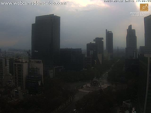 A hazy, overcast city skyline features several tall buildings surrounding a large circular plaza with a fountain.