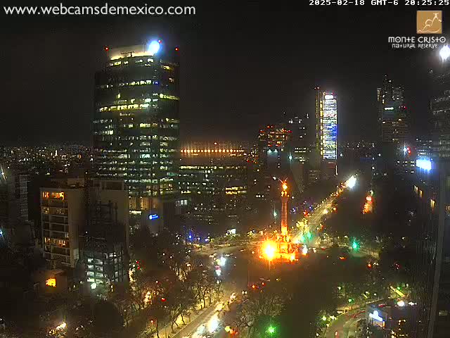 A nighttime aerial view of a city with illuminated buildings and streets surrounding a brightly lit monument.