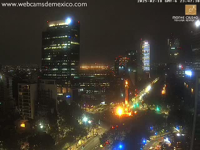 A nighttime aerial view of a city with brightly lit buildings and streets surrounding a monument, under clear skies.
