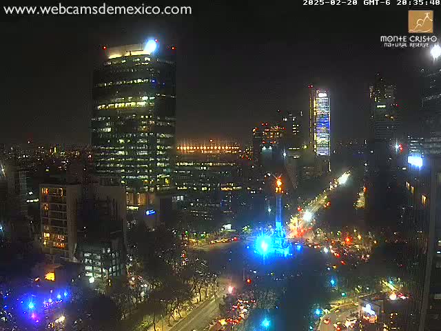 A nighttime aerial view of a city, showing brightly lit skyscrapers and streets with vehicle traffic, under a clear sky.