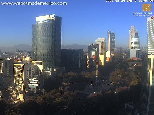 A city skyline with numerous skyscrapers under a clear, sunny sky, featuring a large monument in a central plaza.