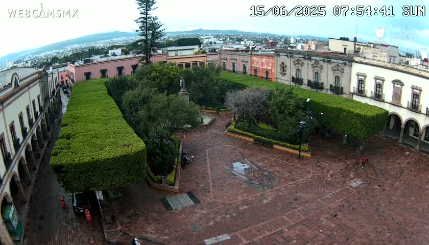 An overcast day reveals a brick plaza with manicured hedges, a central statue, and surrounding colonial-style buildings.