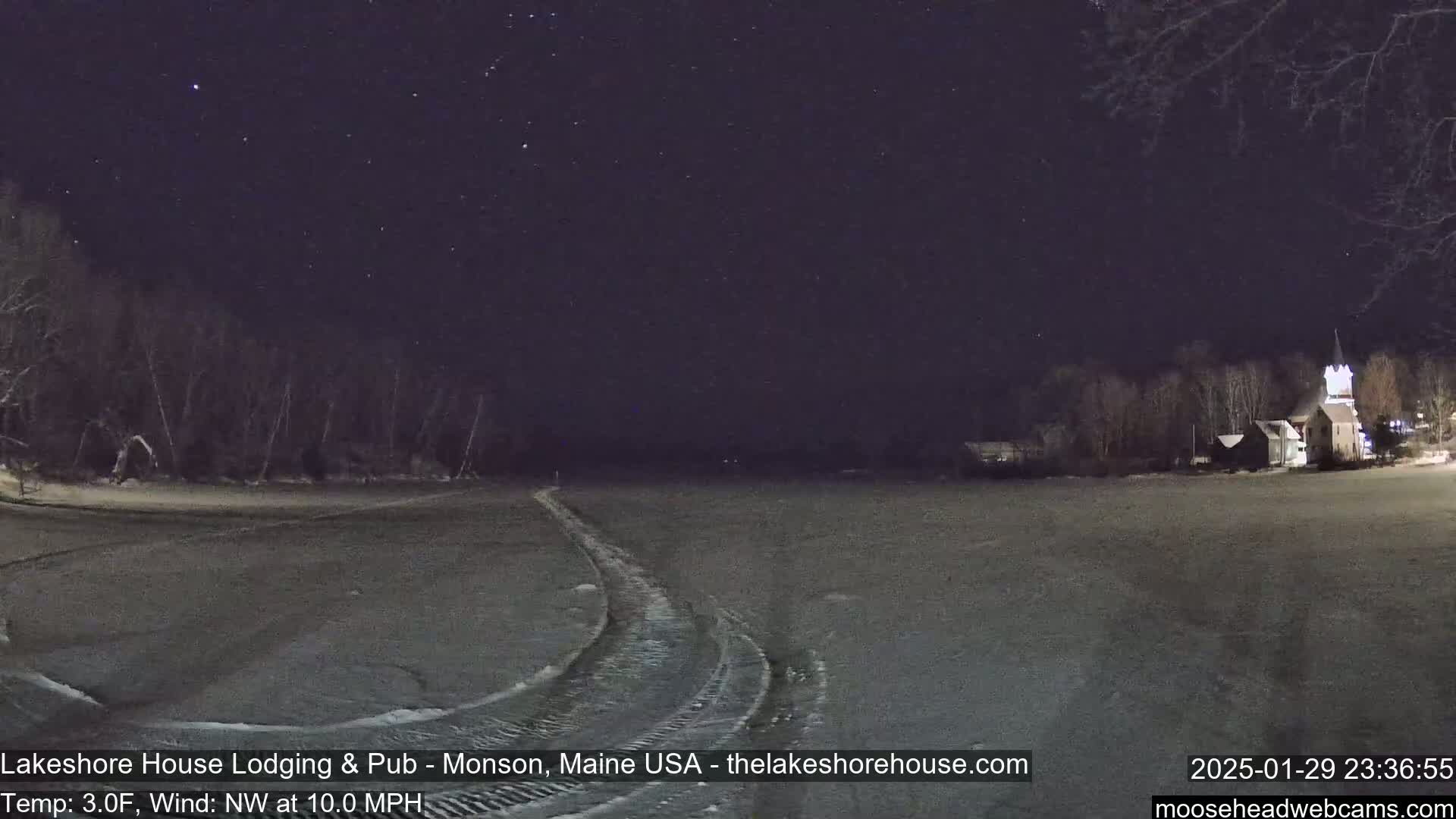 A snow-covered, flat landscape under a clear, starlit night sky shows tire tracks leading to a building in the distance, with a temperature of 3°F and a northwest wind of 10 mph.