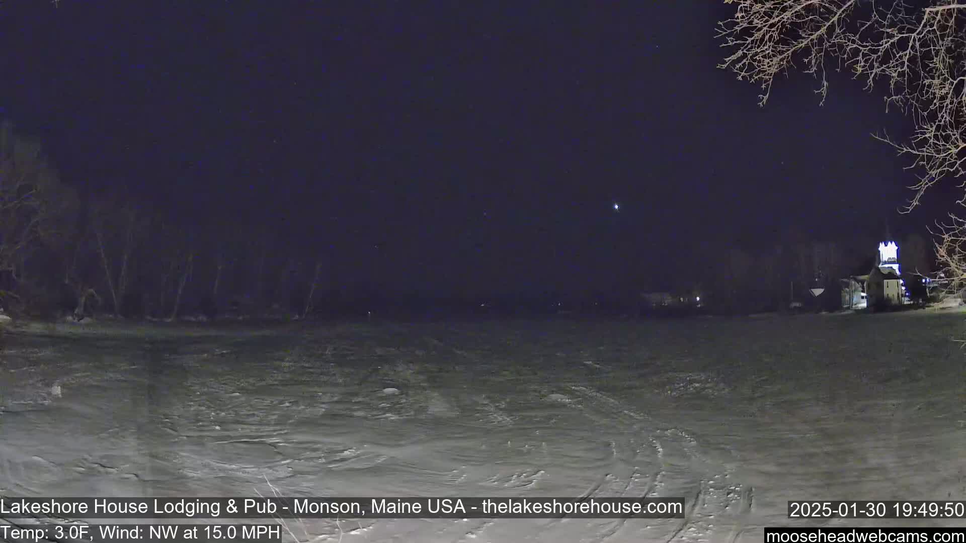 A nighttime view of a snow-covered field with a building and trees in the distance under a starry sky, with a northwest wind at 15 mph and a temperature of 3 degrees Fahrenheit.