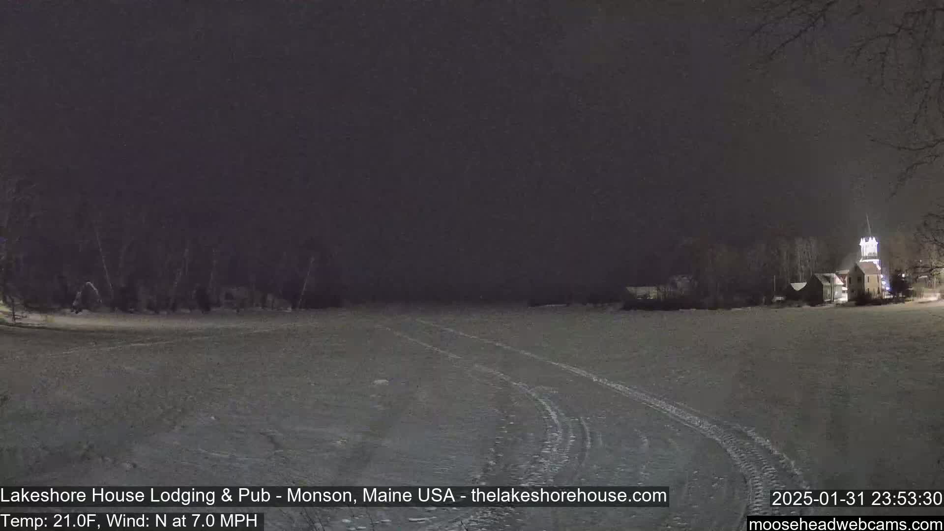 A snow-covered landscape is visible at night, with a building in the distance under a lightly snowing sky.