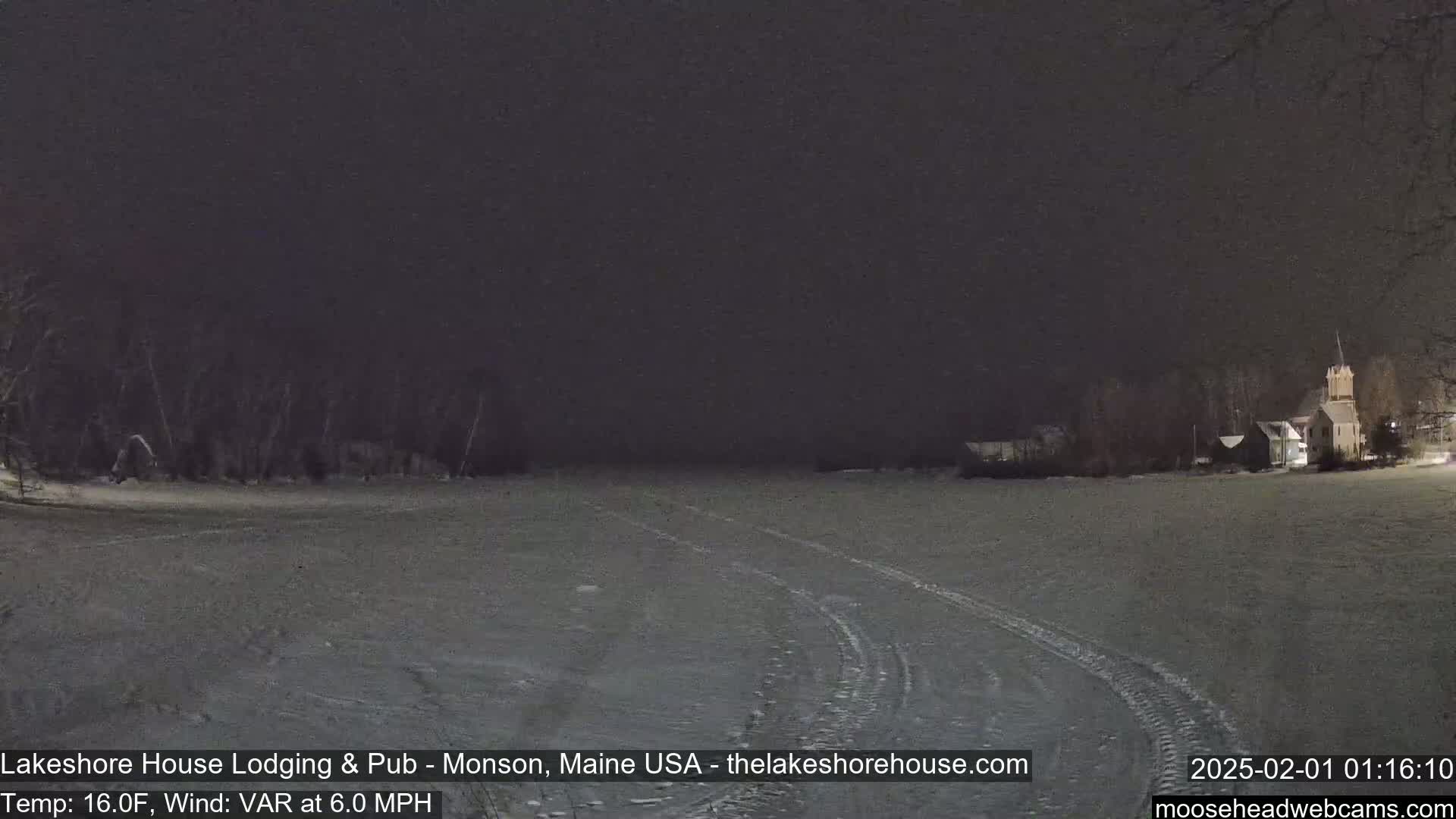 A snow-covered field at night, with a building and trees visible in the distance under a dark sky.