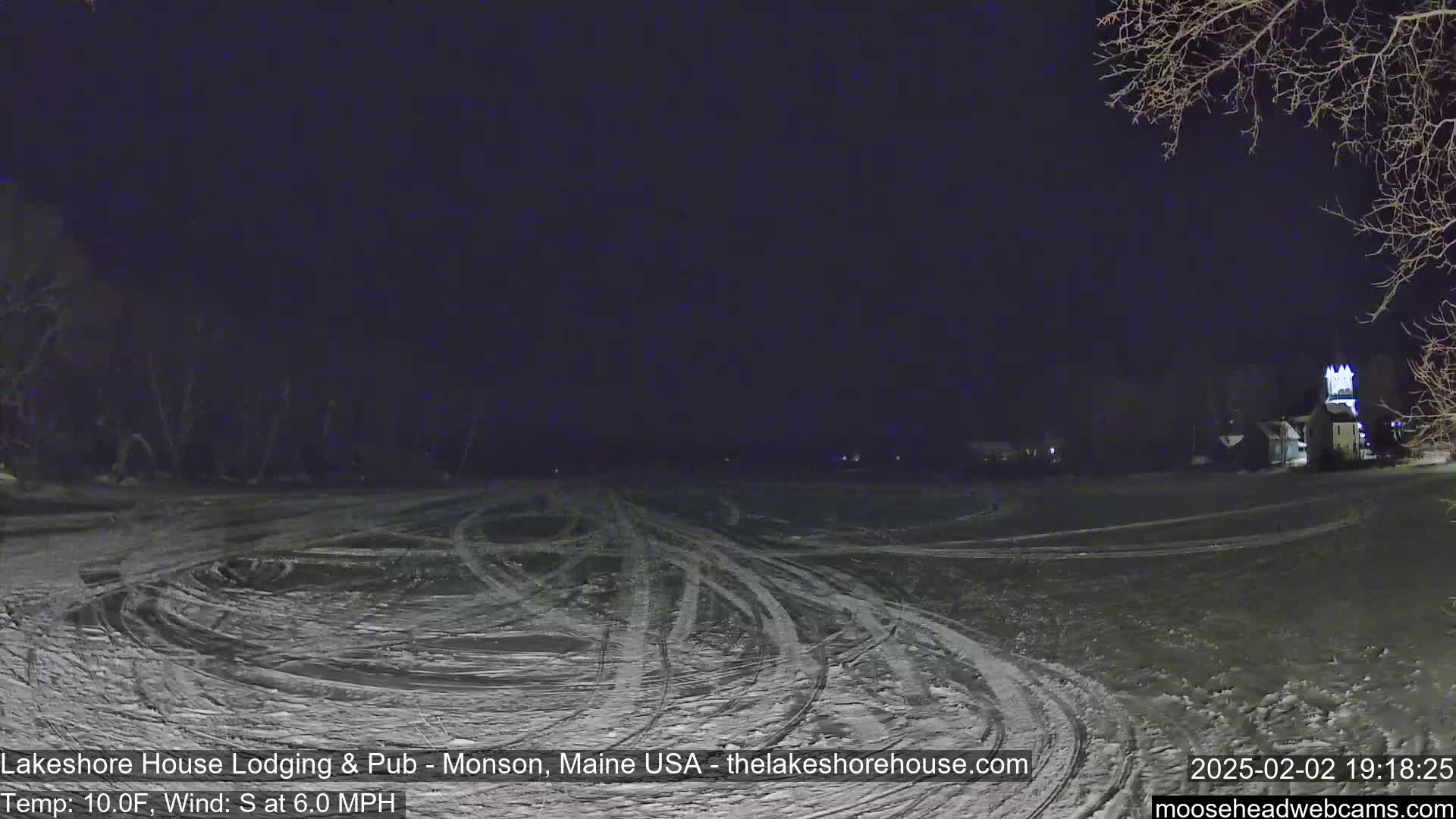 A snow-covered field with tire tracks under a dark night sky, a building faintly visible in the distance.