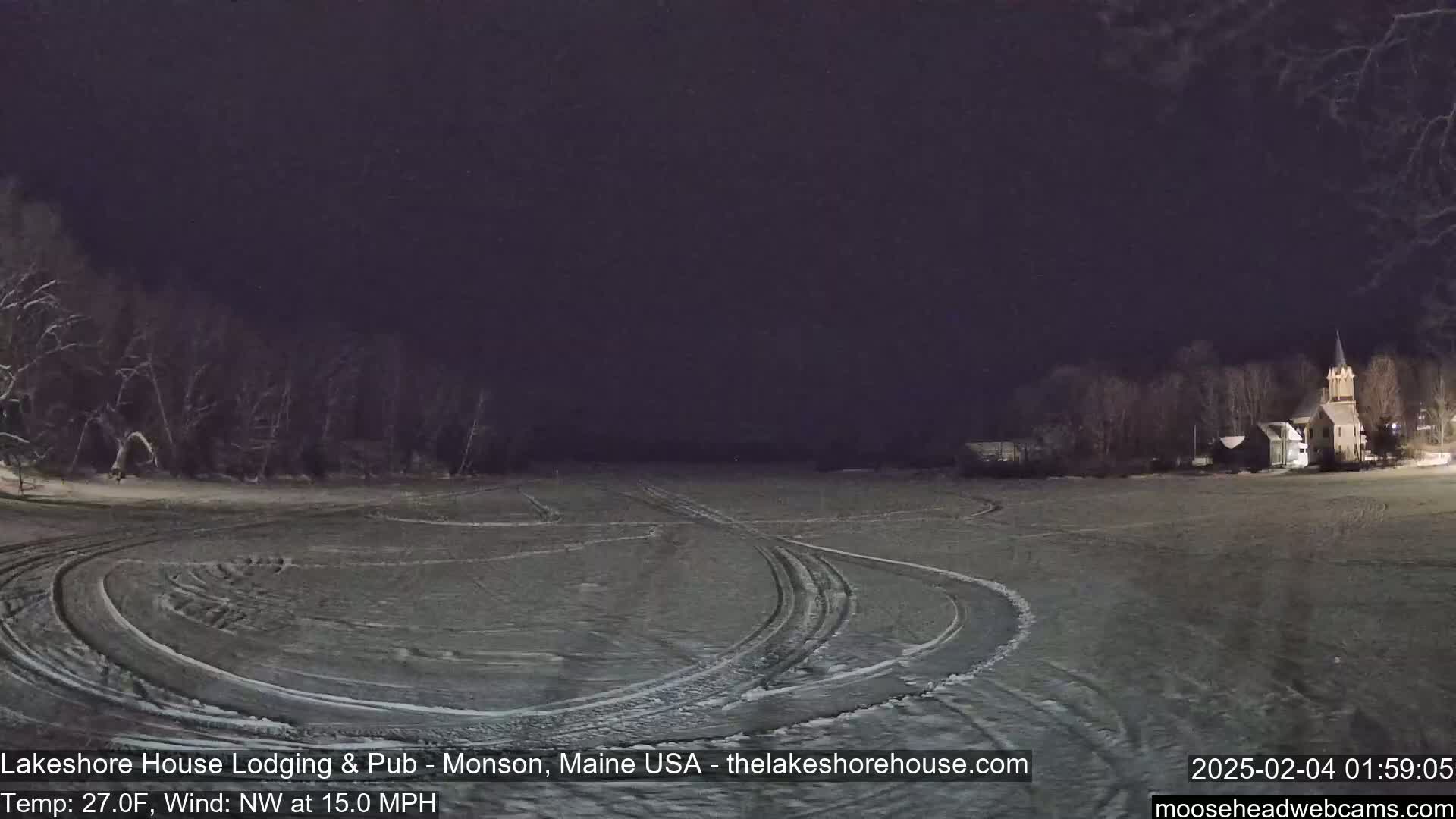 A snow-covered field at night with tire tracks and a church in the distance under a dark sky, with a northwest wind at 15 mph and a temperature of 27 degrees Fahrenheit.