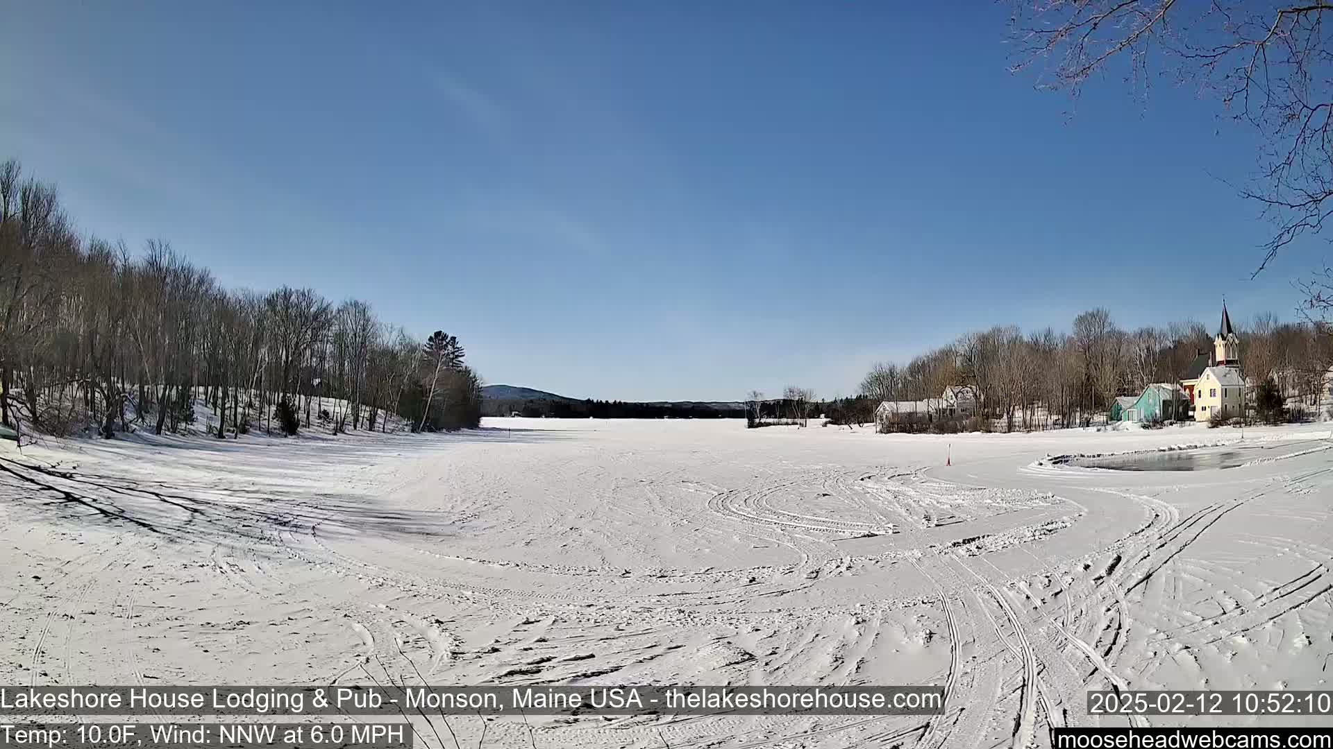 A snow-covered frozen lake stretches out to a small village under a clear blue sky.