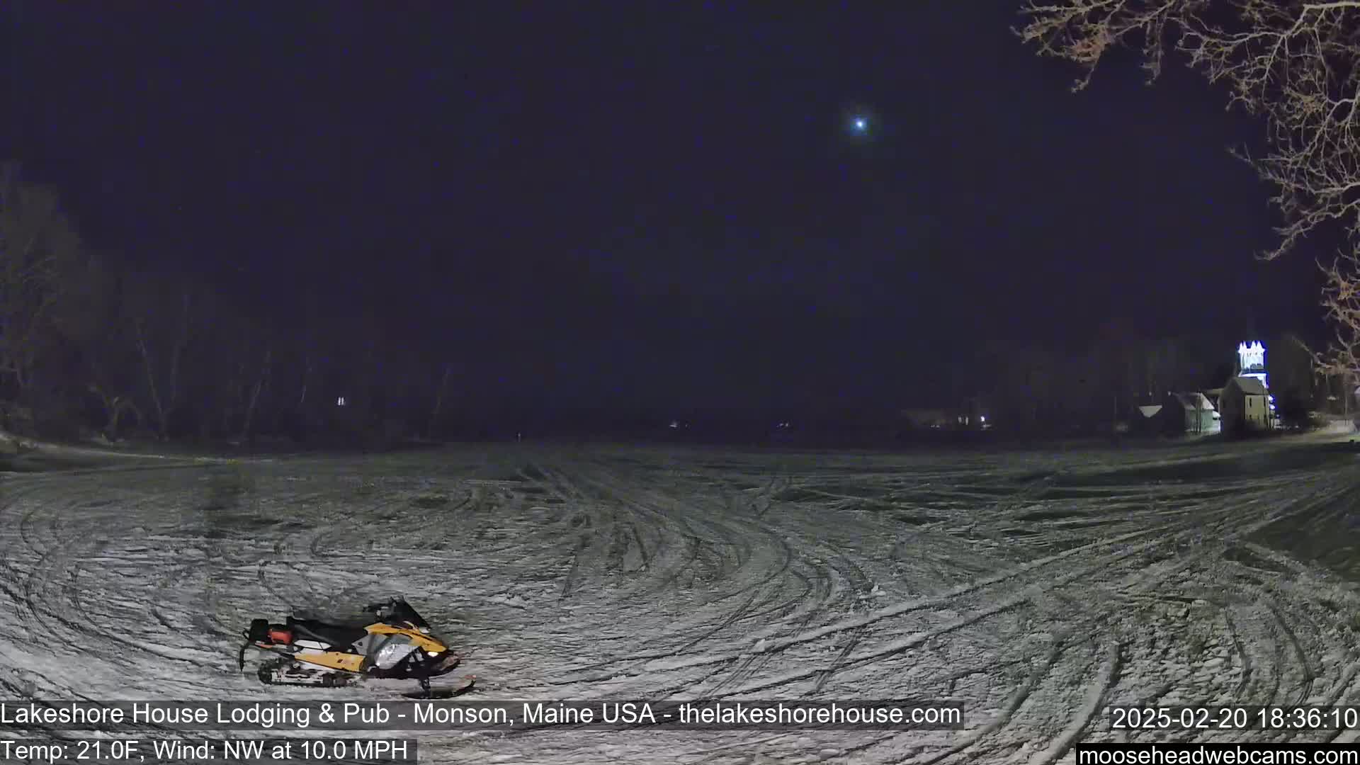 A snowmobile sits on a snow-covered field at night under a dark sky with a bright star visible, with a light wind blowing from the northwest.