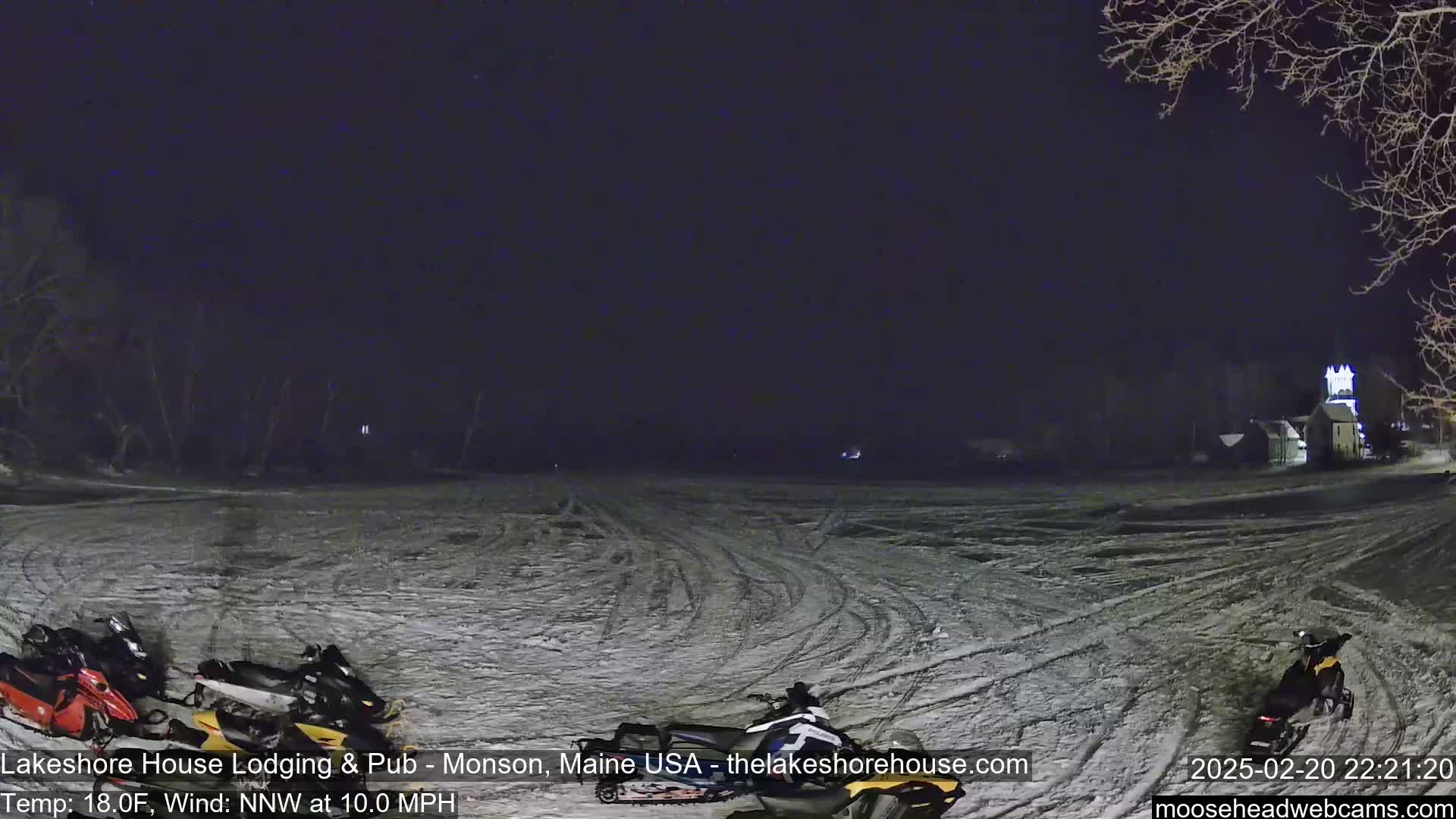 A snow-covered field at night with several snowmobiles parked near the bottom, under a dark, clear sky with a 10 mph north-northwest wind and a temperature of 18 degrees Fahrenheit.
