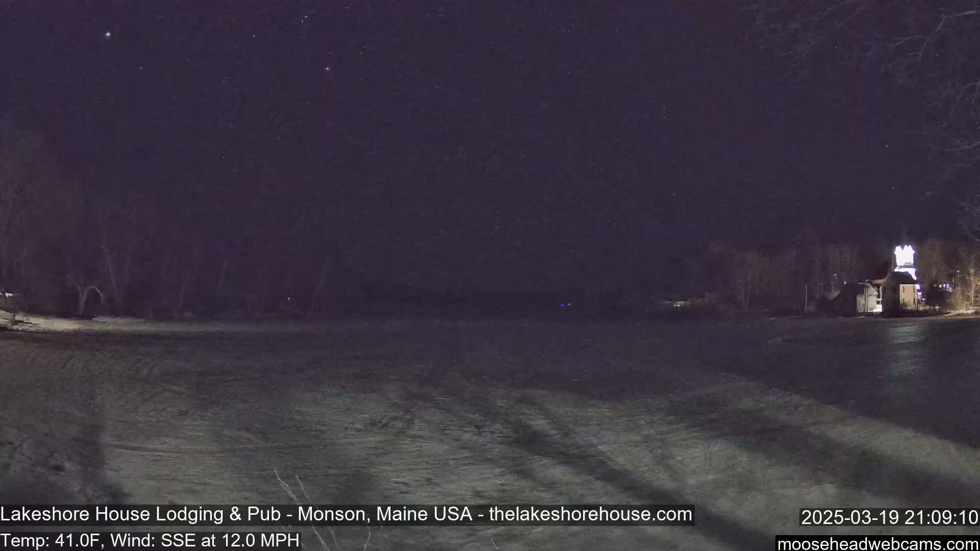 A nighttime scene shows a snow-covered field under a starry sky, with a building illuminated in the distance, and a 12 mph wind blowing from the South-Southeast at a temperature of 41°F.