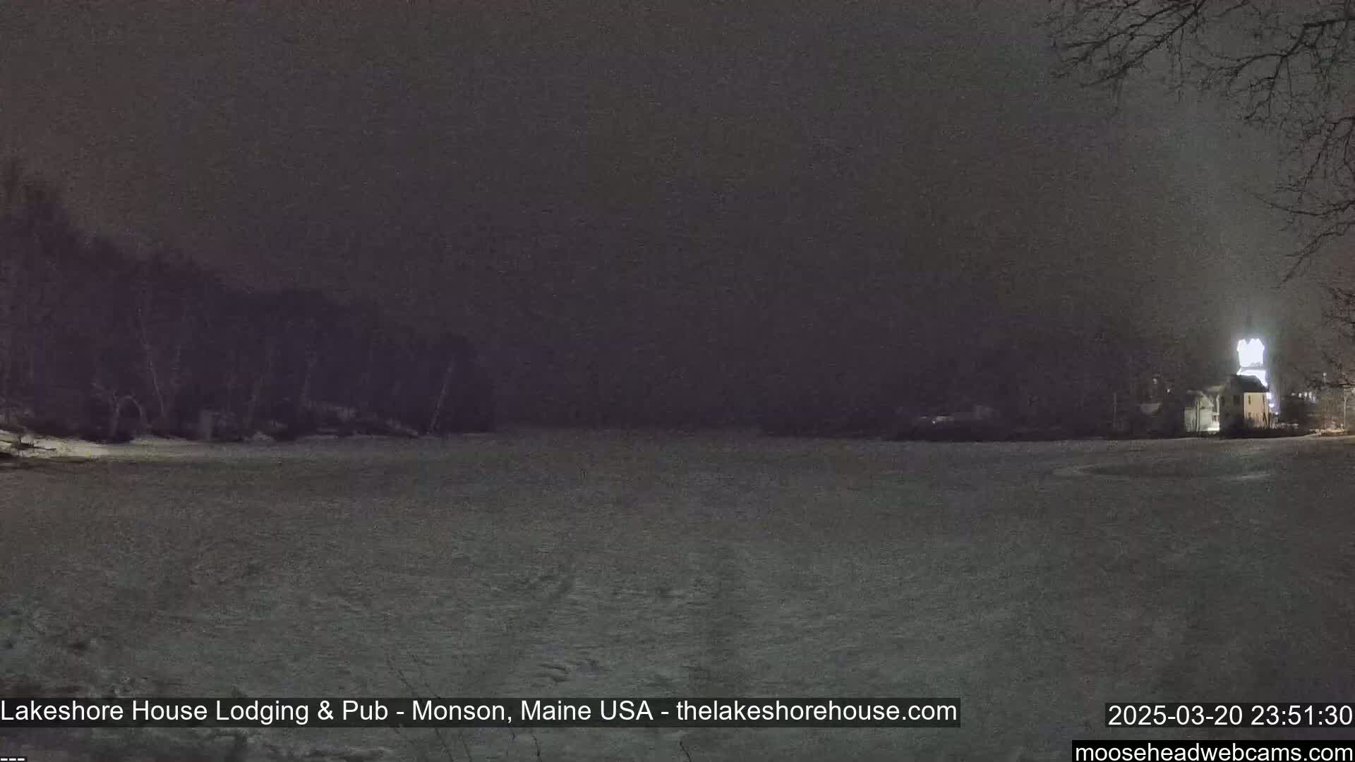 A snow-covered expanse stretches out under a dark, nighttime sky, with a dimly lit building visible in the distance.
