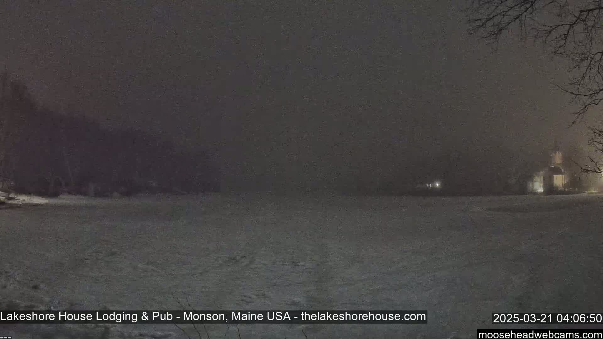 A snow-covered field is visible at night under a dark, foggy sky, with a building faintly illuminated in the distance.