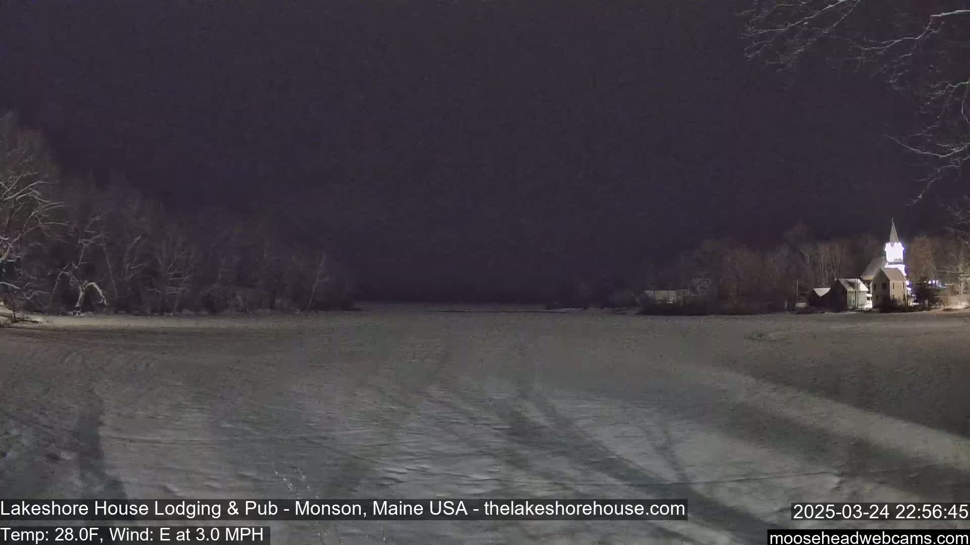 A snow-covered landscape at night, with a church steeple faintly visible in the distance under a dark sky, and a light east wind.