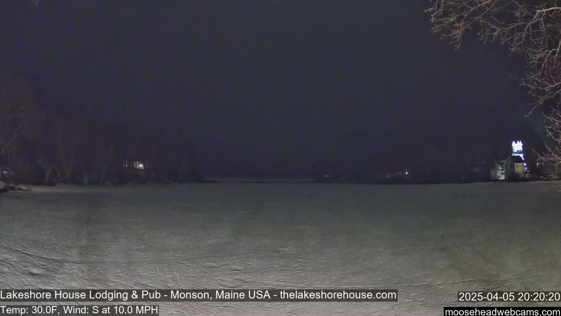 A nighttime view of a snow-covered landscape shows a body of water and buildings in the distance under a dark, clear sky with a 10 mph south wind and a temperature of 30°F.