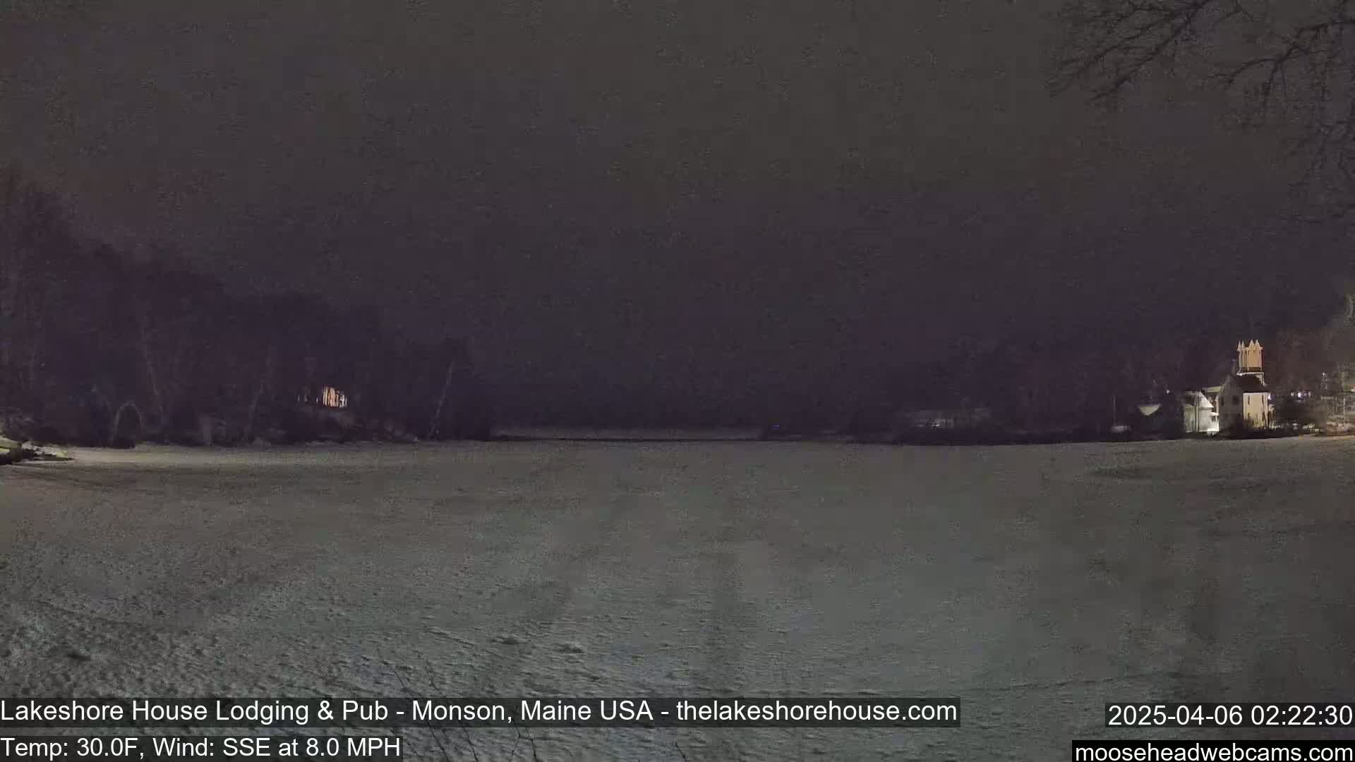A snow-covered landscape is visible at night, with dark trees and buildings in the distance under a dark sky.
