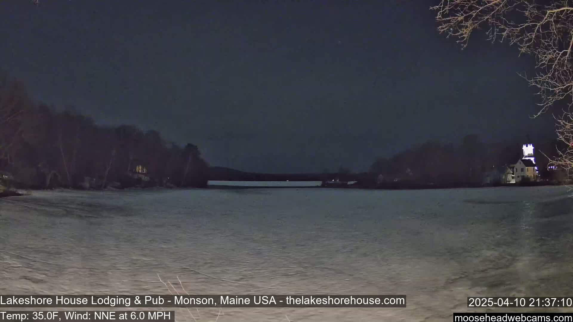 A nighttime view of a partially frozen lake, with a building lit up on the far shore, under a dark sky.