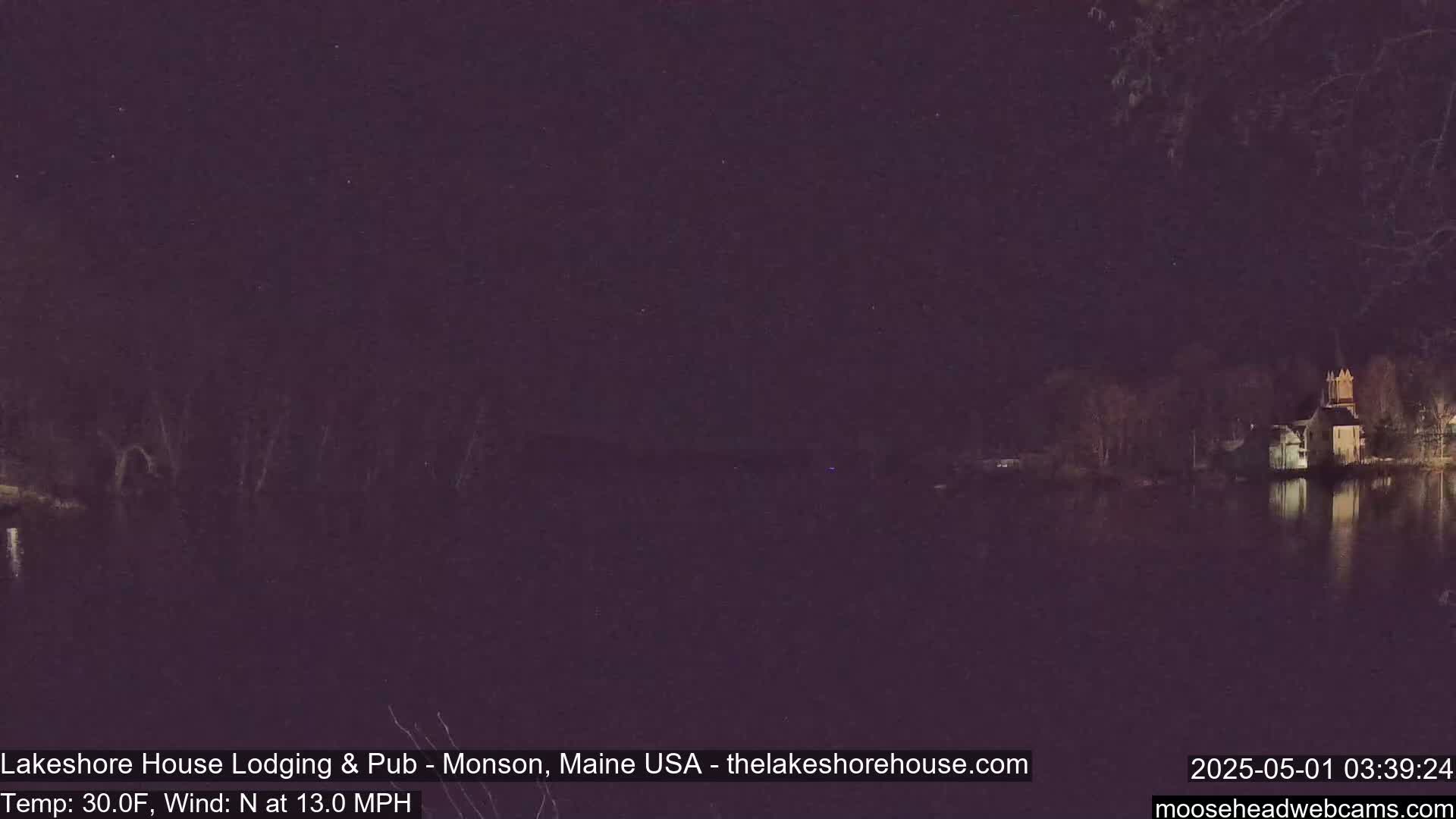 A nighttime view of a calm body of water reflecting a building with a spire under a slightly starry sky, with a north wind of 13 mph and a temperature of 30°F.