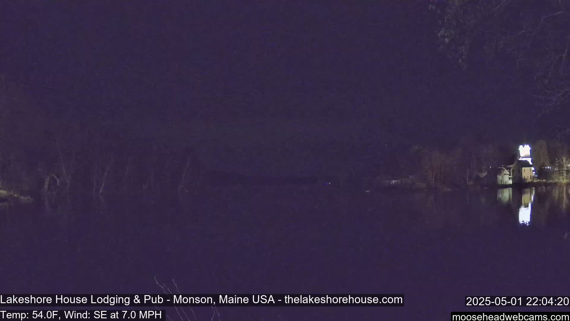 A nighttime view of a calm body of water reflecting a building with lights on, under a dark sky.