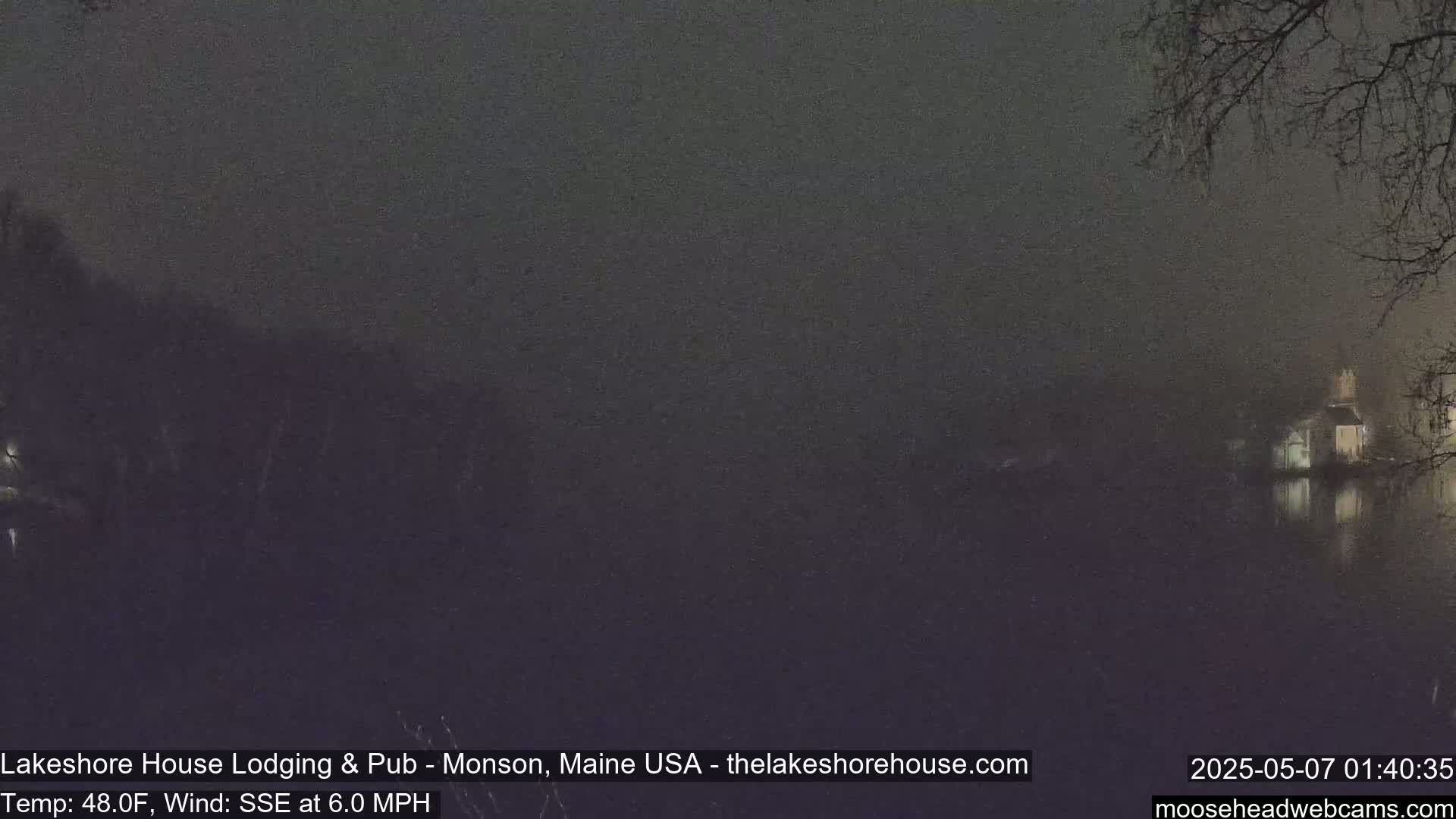 A dark, nighttime scene shows a calm body of water reflecting a dimly lit building under a misty sky.