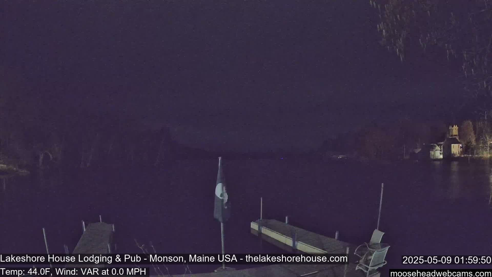 A nighttime view of a calm lake with a dock and a chair, under a dark sky.
