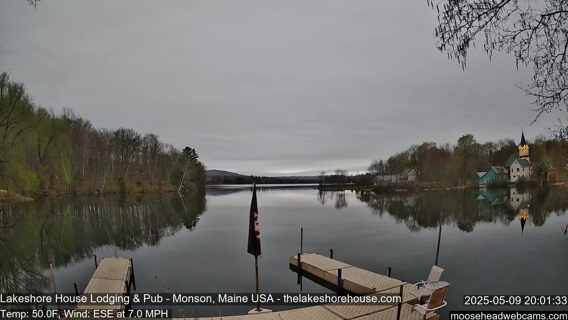 A calm lake reflects a cloudy sky and trees under which sit two docks.