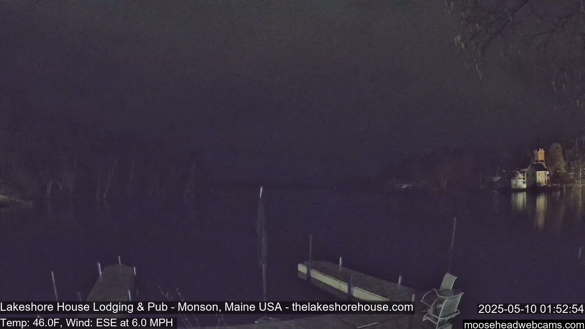 A nighttime view of a calm lake with docks and a building on the opposite shore under a dark sky.