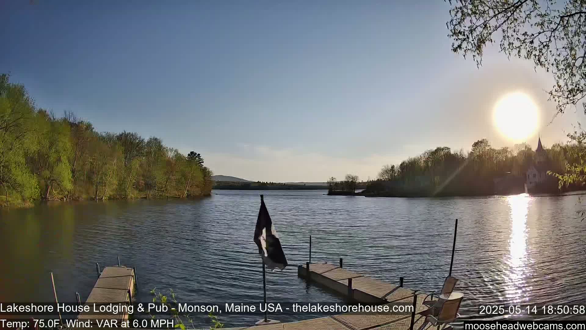 A calm lake at sunset, with a dock, trees lining the shore, and a slight breeze.