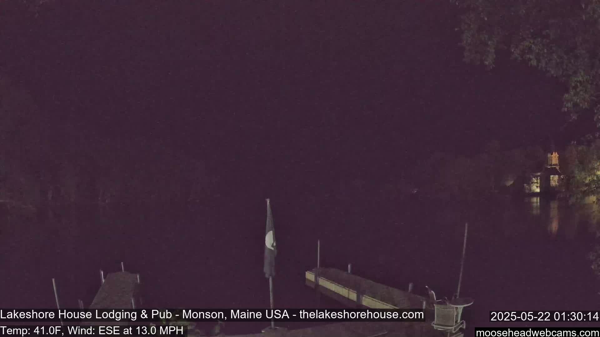 A nighttime view of a dark body of water with a dock and a flagpole, under a dark sky with a 41°F temperature and 13 mph ESE wind.