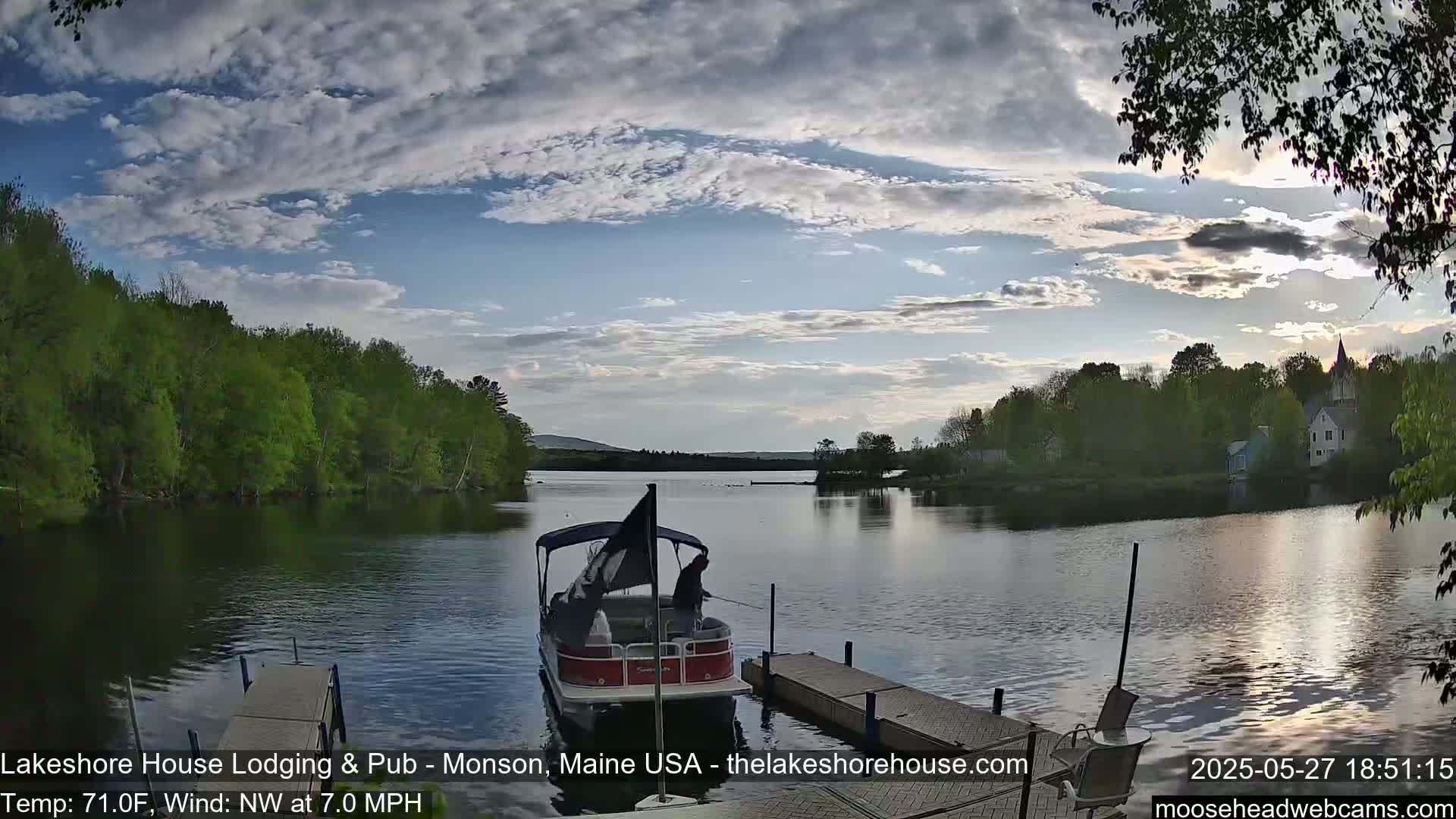 A pontoon boat is docked at a lakeside pier under a partly cloudy sky, with a gentle northwest wind.
