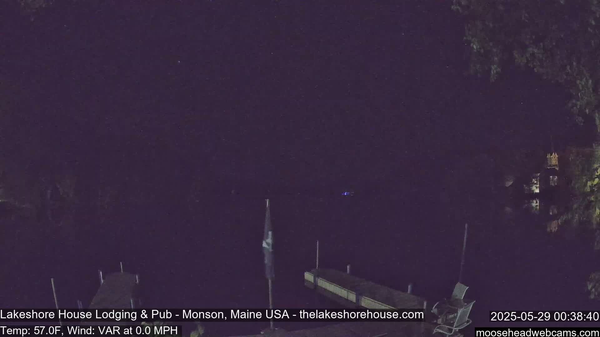 A nighttime view of a dark body of water with a dock and a flagpole, under a clear, starry sky.