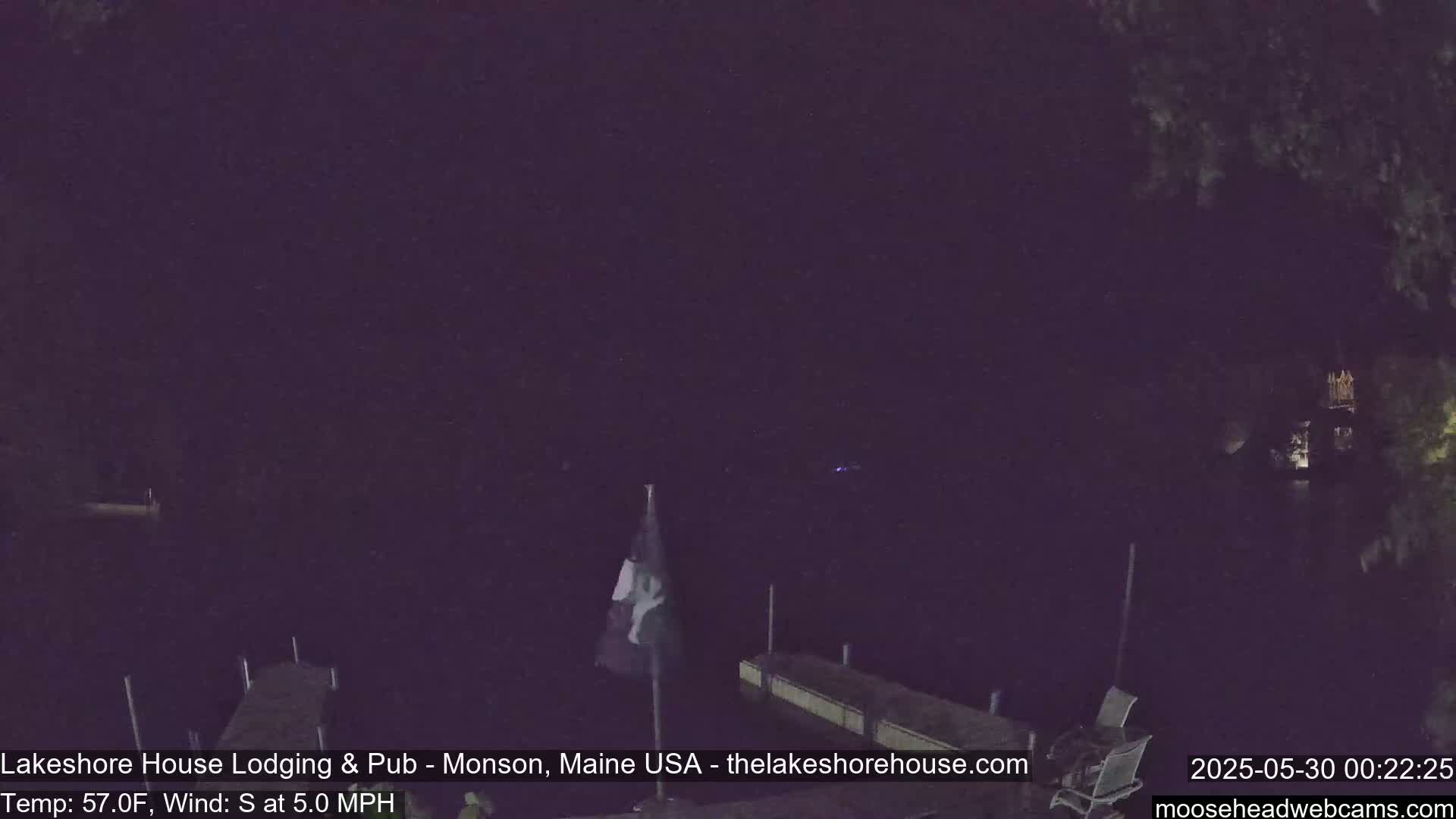 A nighttime view of a dark body of water with a flag hanging limply on a pole near a dock, under a dark sky with a 5 mph south wind and a temperature of 57°F.