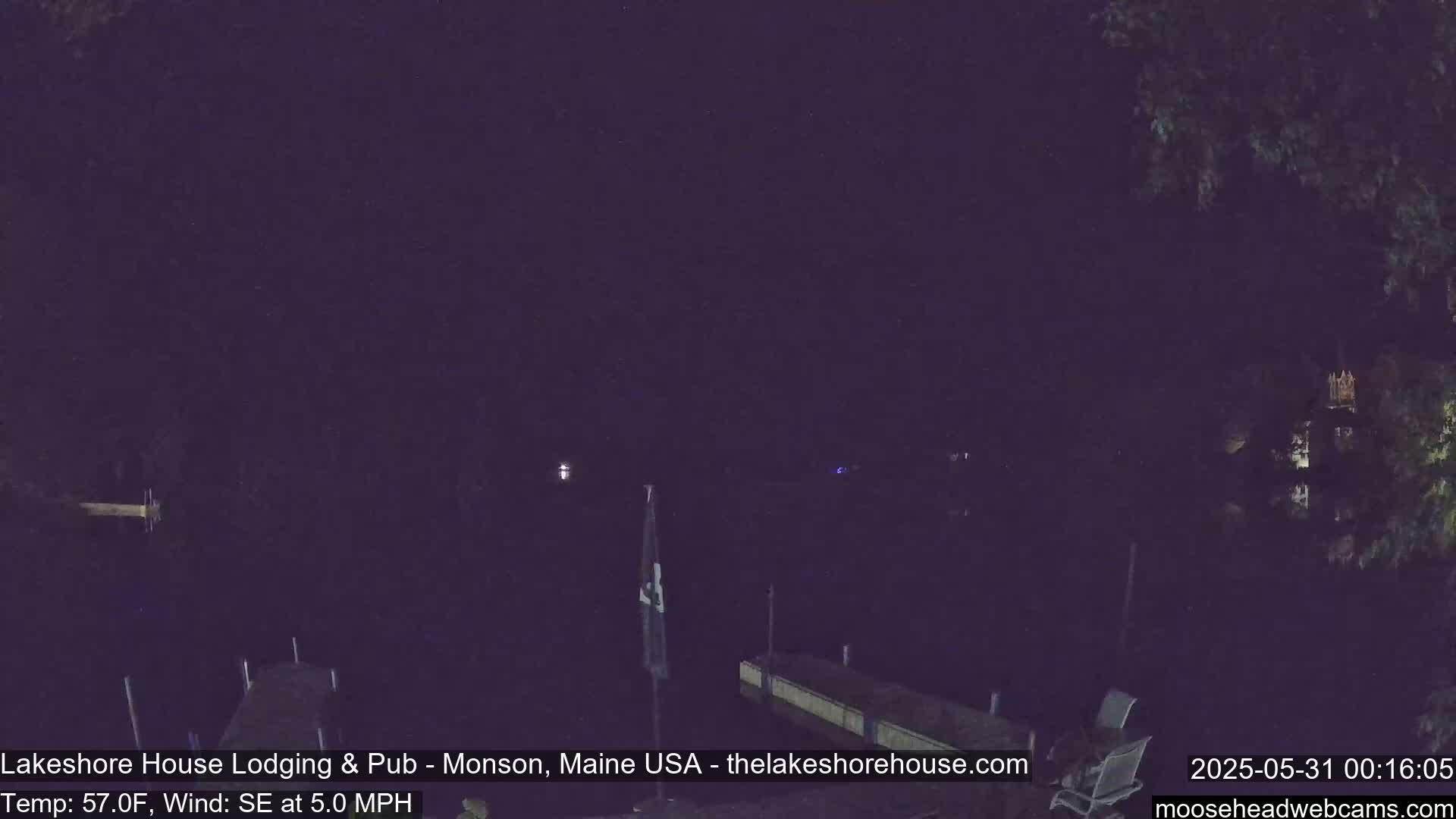 A nighttime view of a dark body of water with a dock and some trees in the background, under a dark sky with a southeast wind.