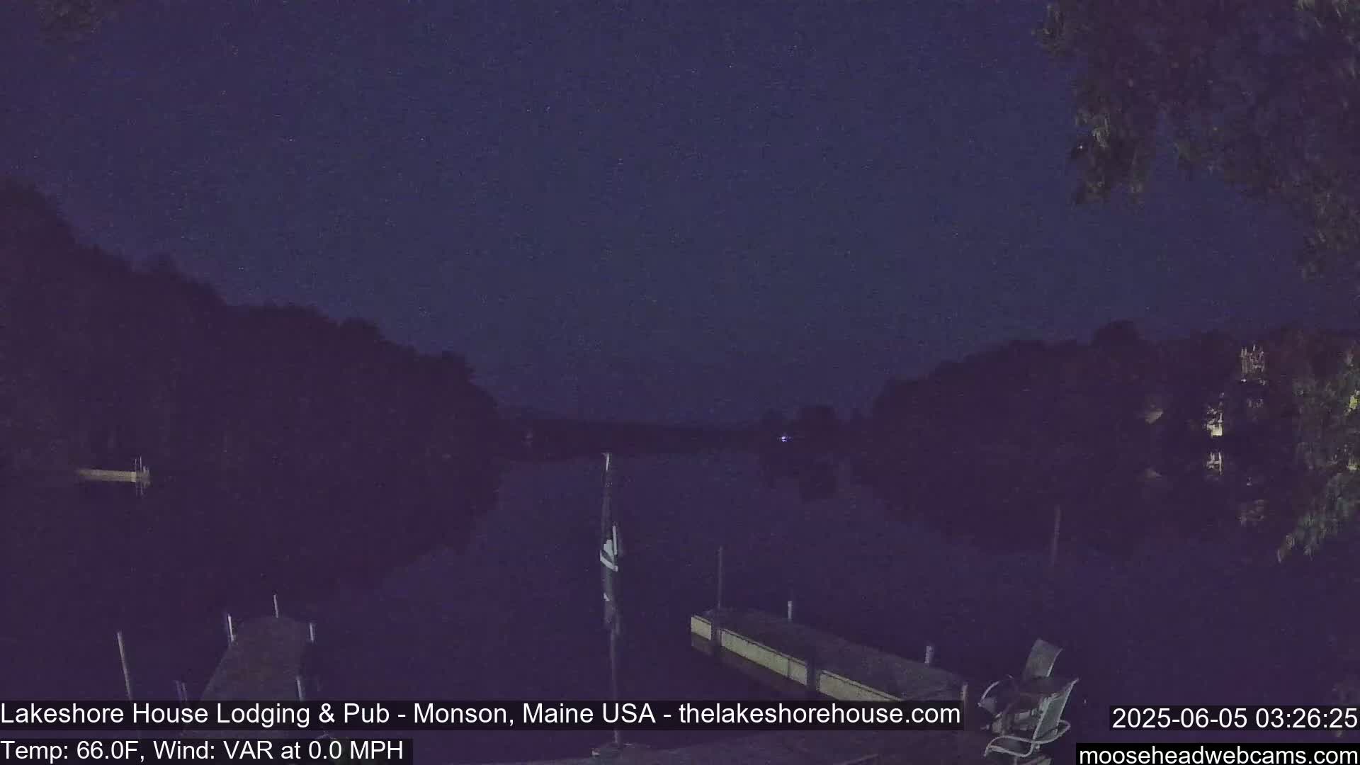 A nighttime view of a calm lake with a dock, under a dark, starlit sky.