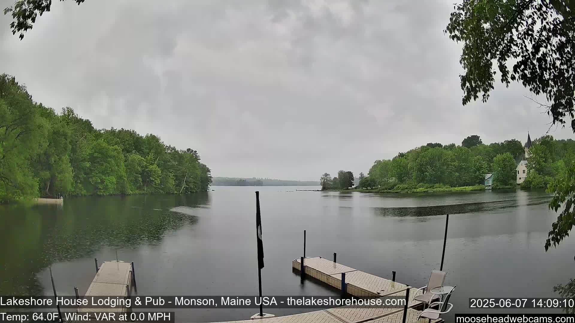 A calm lake is viewed from a dock under an overcast sky with light rain.