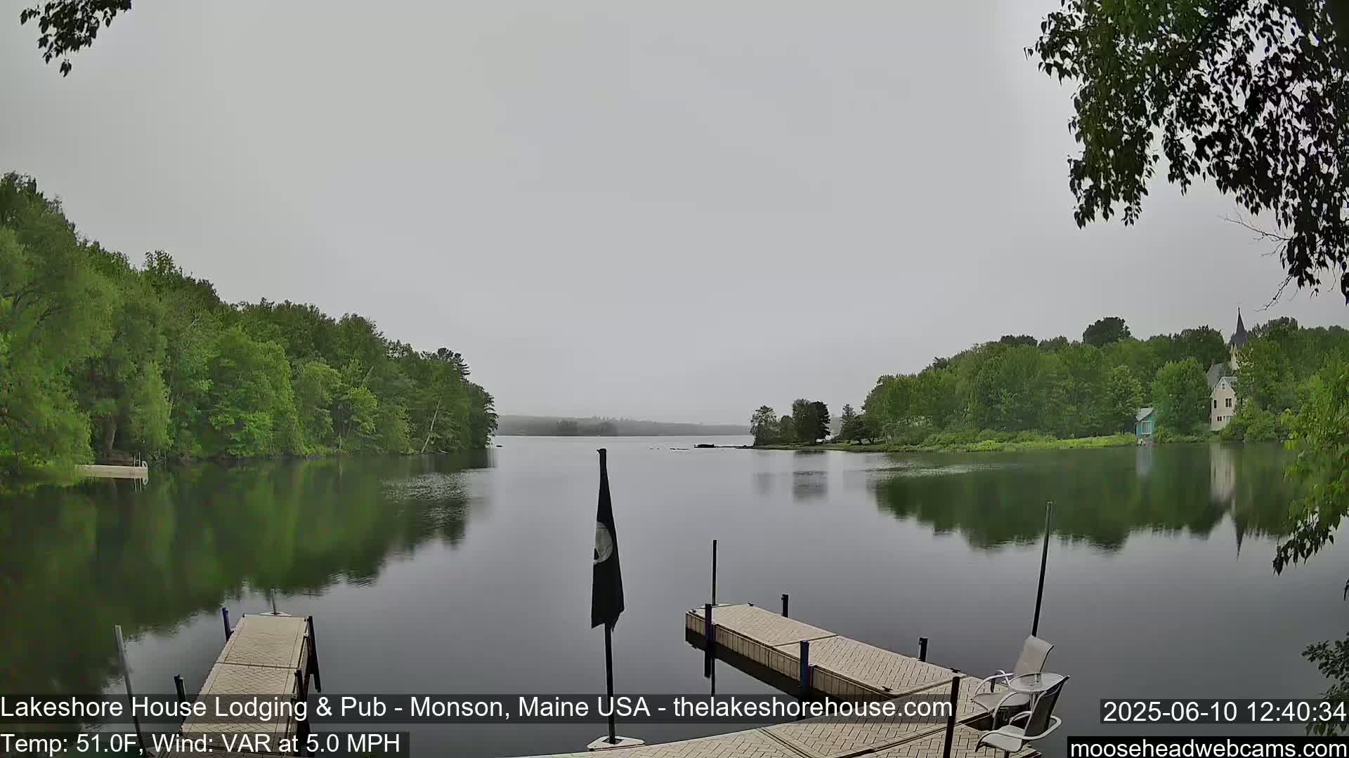 A calm lake reflecting a gray sky and lush green trees, with two wooden docks in the foreground.