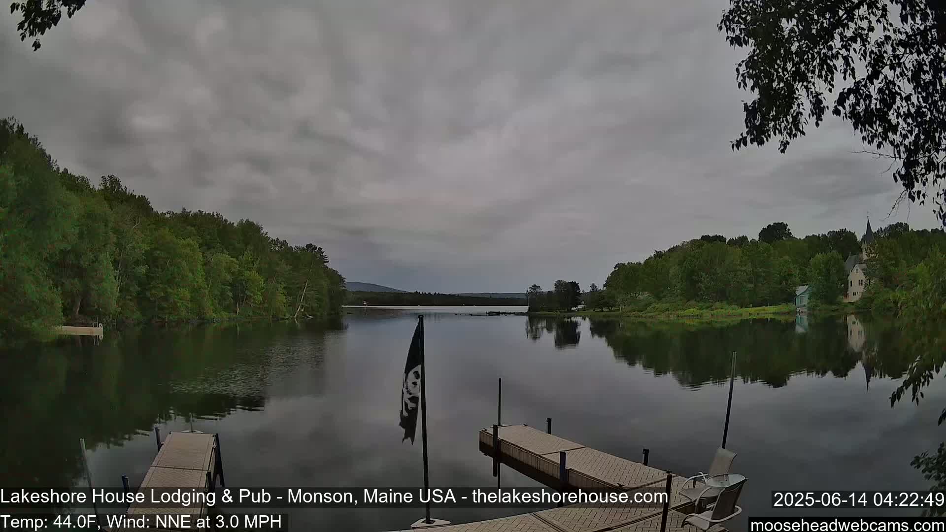 A calm lake with a wooden dock and trees lining the shore under an overcast sky.